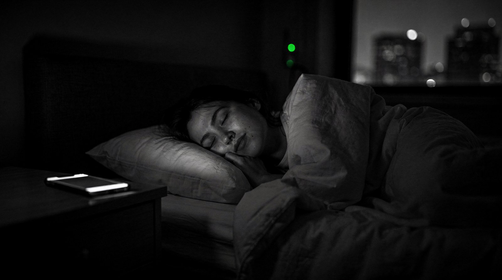 A person sleeps peacefully at night; the phone on the nightstand stays dark, one small green status light glows in the room